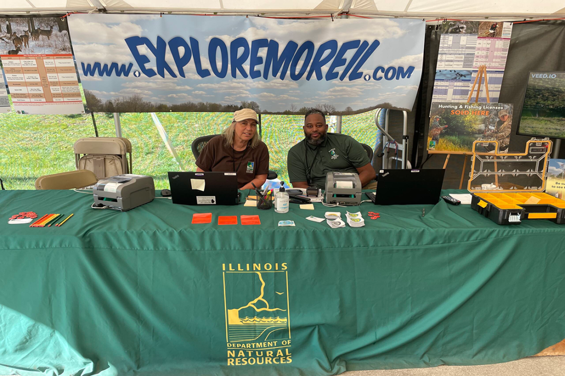 Two IDNR employees work the licensing table in Conservation World, where customers can purchase their license for the year.